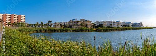 Destin, Florida- Panorama of lagoon with tall grass on the shore in a residential area. There is an apartment building on the left and three-storey homes on the right near the lagoon.