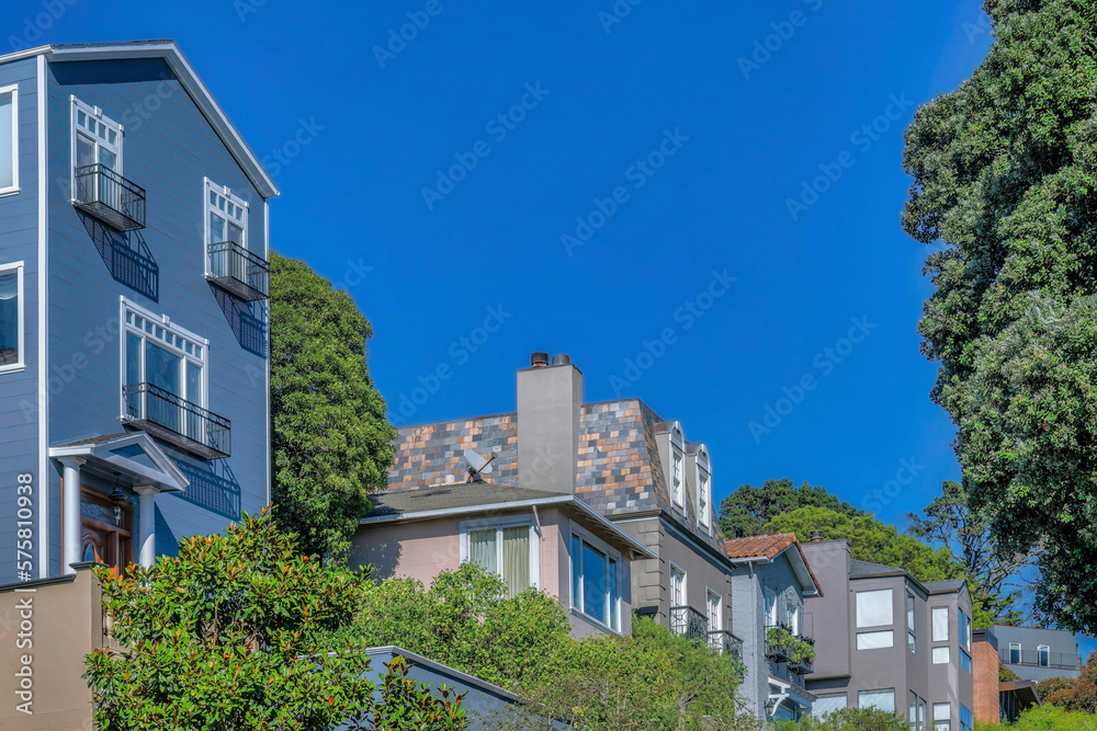 Multi storey houses on a sunny day in San Francisco California residential area.. Facade of homes on a bright neighborhood viewed from the street against blue sky background.