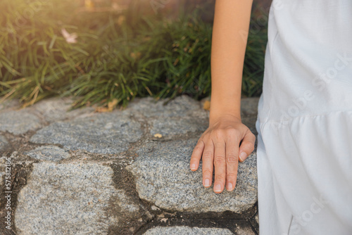 Close-up view, woman wearing white dress sitting on rock wall in resort educating, relaxing happily. concept about of relax, holiday, resort, comfort.