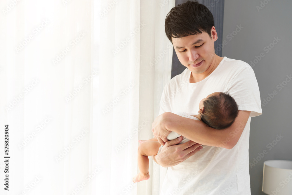 father holding and looking his newborn baby near window in bedroom