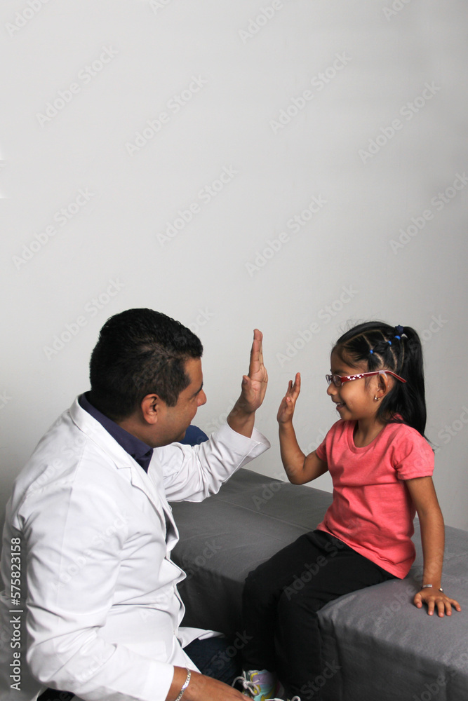 Pediatrician doctor and 4 year old latin girl patient in consultation are friends and make hi five sign and bump fists
