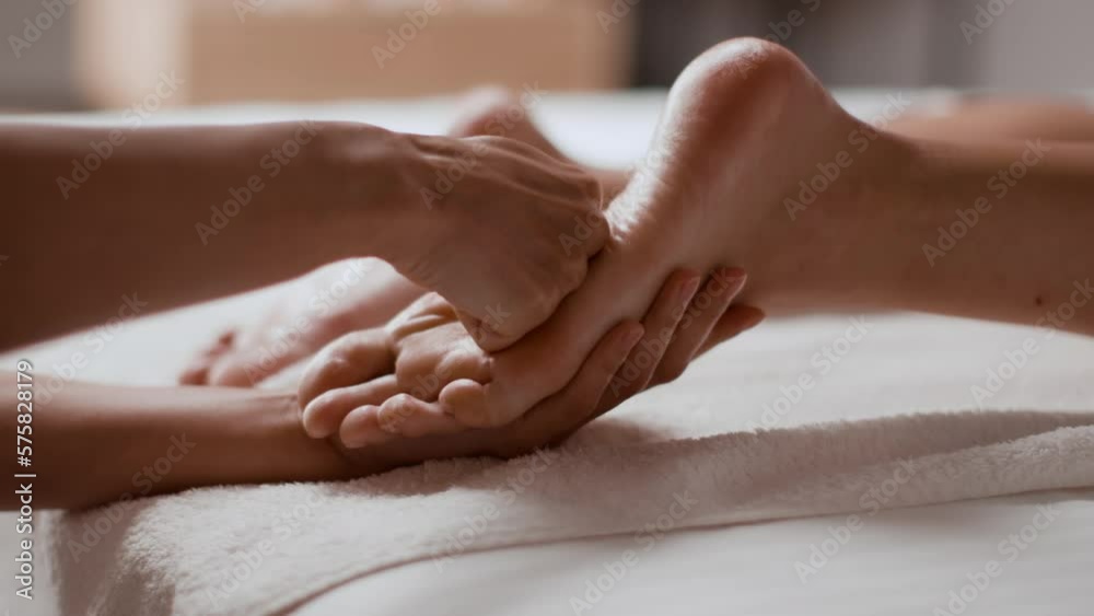 Young woman getting leg and feet massage in resort spa salon, unrecognizable masseur rubbing female foot, slow motion