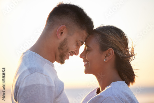 Couple, sunset forehead touch for love, outdoor beach date and happy holiday together. Man, woman and face of relationship at ocean for freedom, support and relax with trust, peace and smile of care