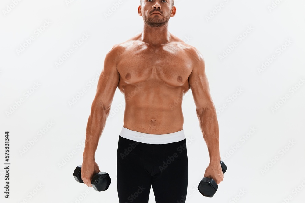 Man athletic body bodybuilder posing with dumbbells with naked torso abs full-length in the background, fitness class. Advertising, sports, active lifestyle, competition, challenge concept. Man athletic body bodybuilder posing with dumbbells with naked torso abs full-length in the background, fitness class. Advertising, sports, active lifestyle, competition, challenge concept.