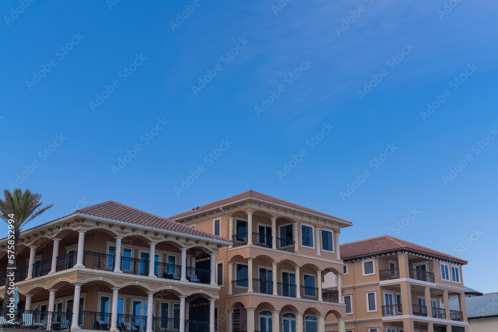 Three villas with pillars on balconies in Destin, Florida. Low angle view of resort villas in a row with clear blue sky background.