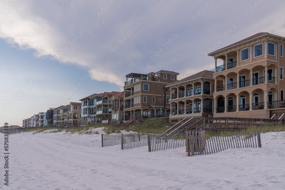 Row of beach houses and resort villas in Destin, Florida. White sand shore and fenced sand dunes at the front of the building with footbridges access to the beach.