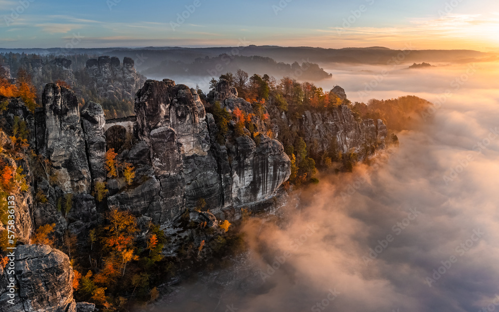 Saxon, Germany - Aerial panoramic view of the Bastei on a foggy autumn morning with colorful autumn foliage and heavy fog under the rock. Bastei is a rock formation in Saxon Switzerland National Park