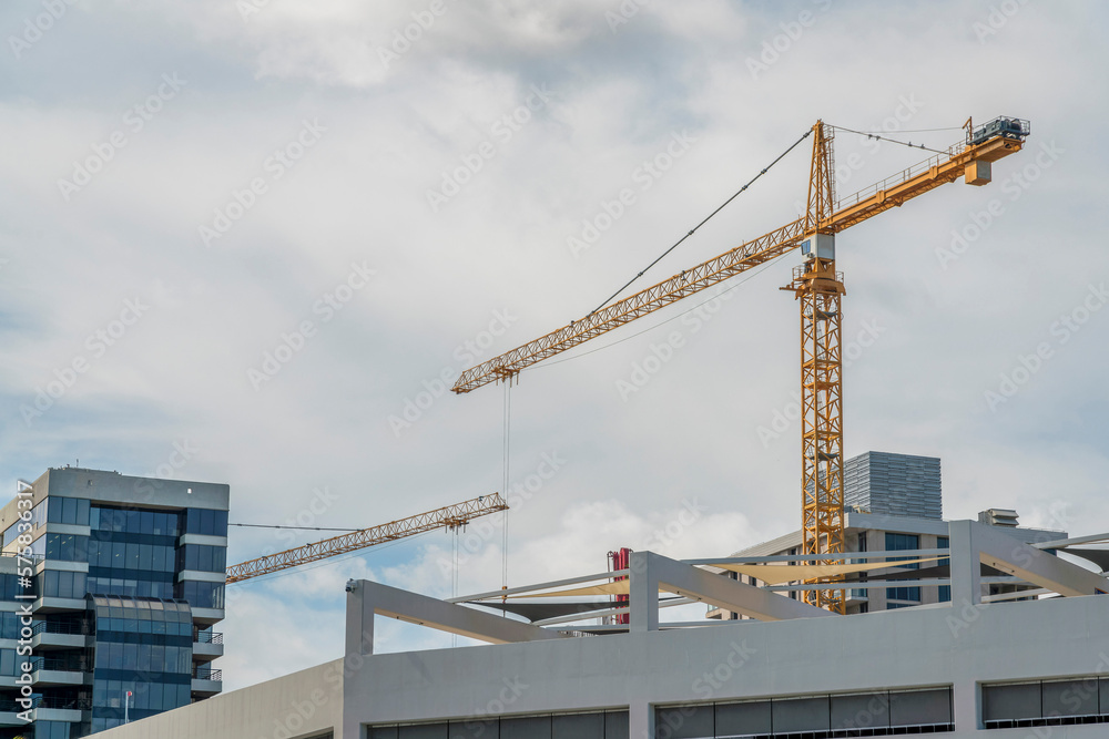 Tower cranes above the multi-storey buildings at Miami, Florida. There is a building on the left with glass window walls near the yellow towers against the white sky background. Tower cranes above the multi-storey buildings at Miami, Florida. There is a building on the left with glass window walls near the yellow towers against the white sky background.