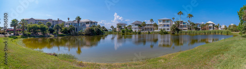 Panorama of waterfront houses overlooking a freshwater lake in Destin Florida. Scenic residential landscape with homes, grassy field, water, and blue sky on a sunny day.