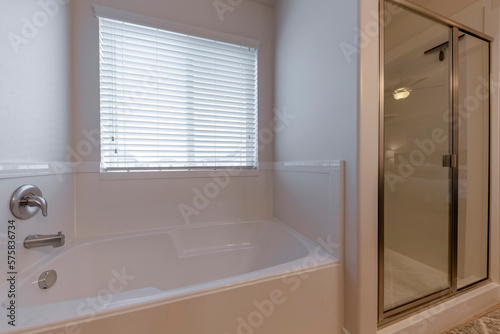 Acrylic bathtub with window beside the shower stall with glass door. There is a bathtub on the left with natural light passage from the window beside the shower stall on the right.