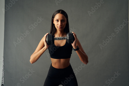 Focused young biracial woman in sports bra and leggings holding weights in studio