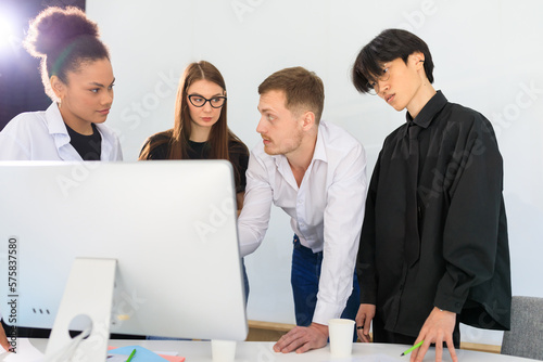 A multinational team stands in front of a computer in the office
