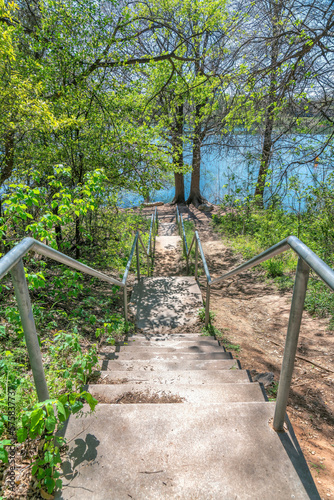 Top of a stairs on a slope with views of trees and Colorado River below- Austin, Texas. Staircase with landings and metal bar handrails in the middle of the woods.
