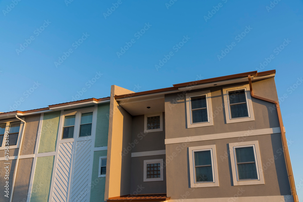 Low angle view of townhouse apartments with box structure at Destin, Florida. View of townhomes facade with gray and green walls with trims under the clear blue sky background.