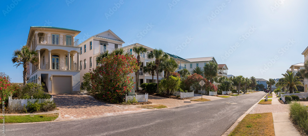 Destin, Florida- Panorama of a street in a neighborhood with three-storey residences. There is a road in the middle of the houses with bricks driveway, fence, and sidewalks outside.