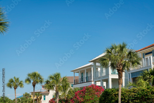 Views of houses with bougainvillea and palm trees at the front in Destin, Florida. Row of houses with balconies under the clear blue skies.