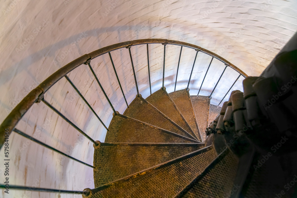 Fototapeta premium Spiral stairs inside Cape Florida Lighthouse in Bill Baggs Cape Florida State Park- Miami, Florida. Perspective view of a rusty spiral stairs heading downstairs beside the painted white bricks wall.