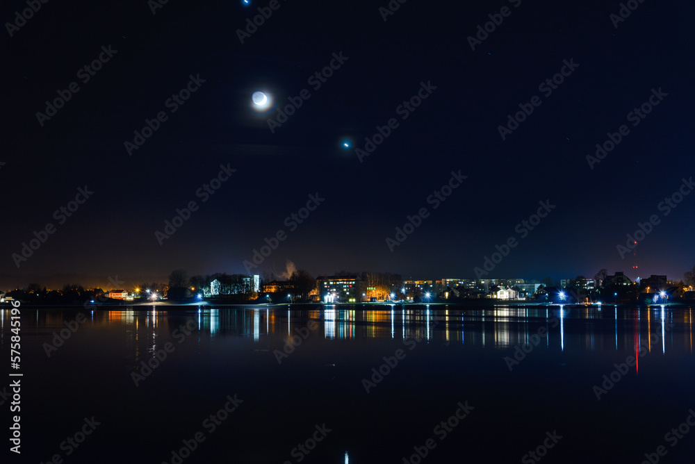 Telsiai town,water,moon night lake in Lithuania. Nice view winter of colorful houses on coast of frozen Lake.Nice winter night.Town colorful light reflections on water.Long exposure.