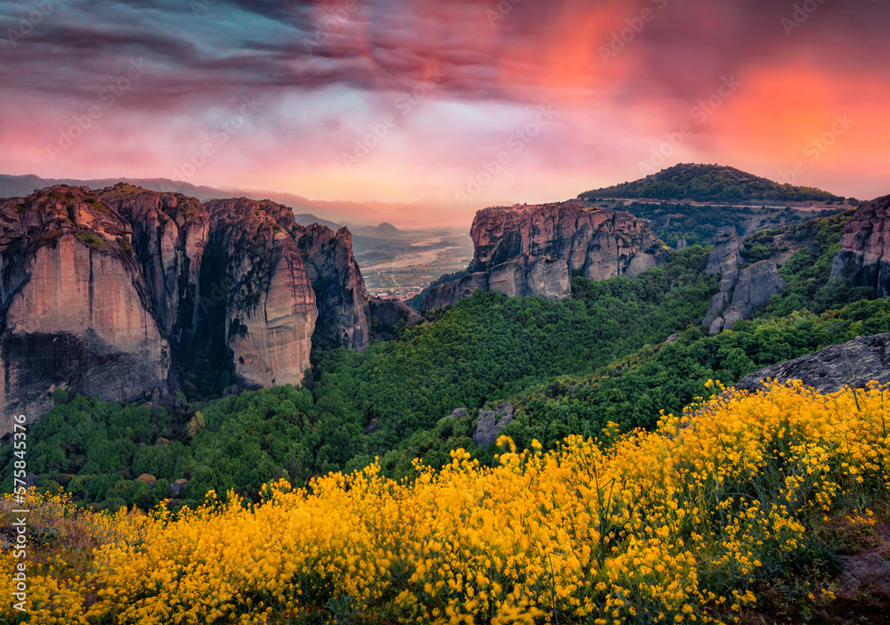 Stunning sunset in Greece. Colorful summer view of famous Eastern Orthodox monasteries, World Heritage site, built on top of rock pillars. Blooming yellow flowers in Kalabaka, Trikala, Thessaly.