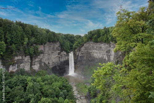 Taughannock Falls on a sunny day, surrounded by rock faces and trees, the watercourse emptying into a pool.
