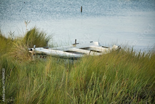 A small wooden boat at anchor in a lush green meadow, the sea in the background.