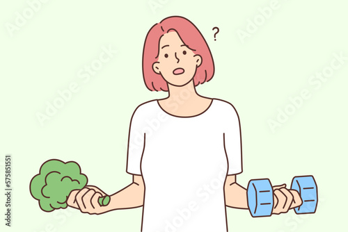 Woman holding dumbbells and broccoli wanting to choose way to lose weight