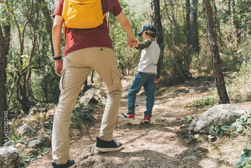 Close-up rear view of tourists school boy and his dad walking a stone footpath in spring forest. Child kid and father wearing casual clothes while hiking in summer greenwood forest.