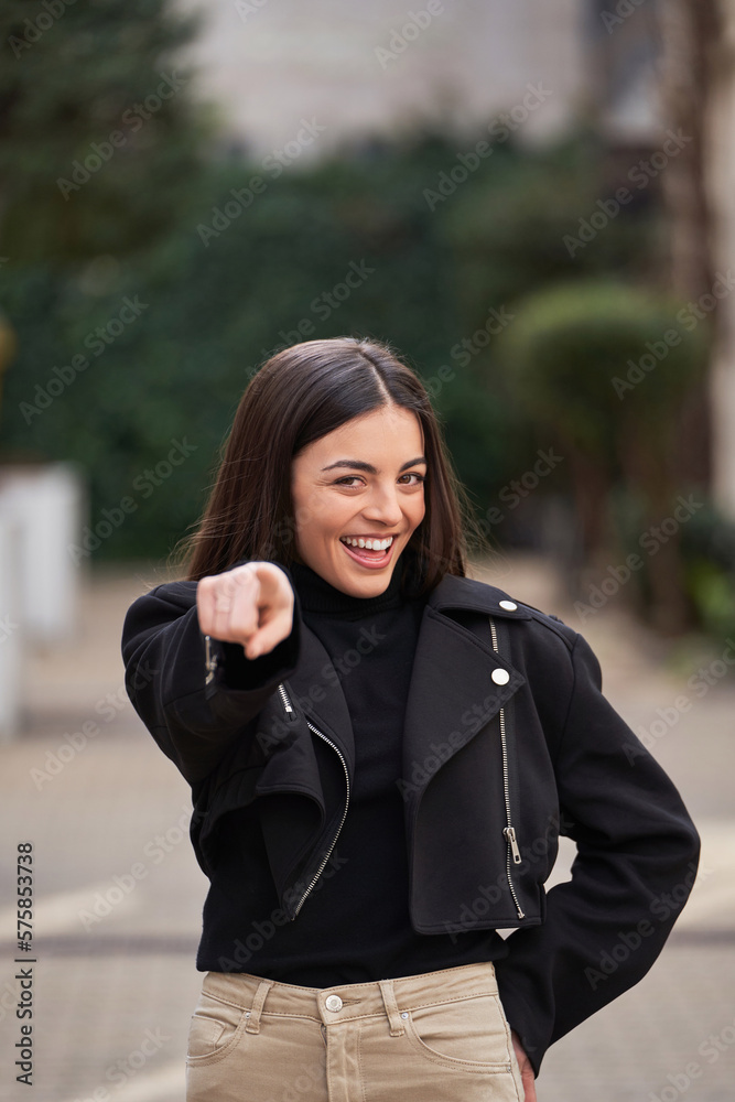 Woman pointing at the camera and smiling while standing outdoors. Woman pointing at the camera and smiling while standing outdoors.
