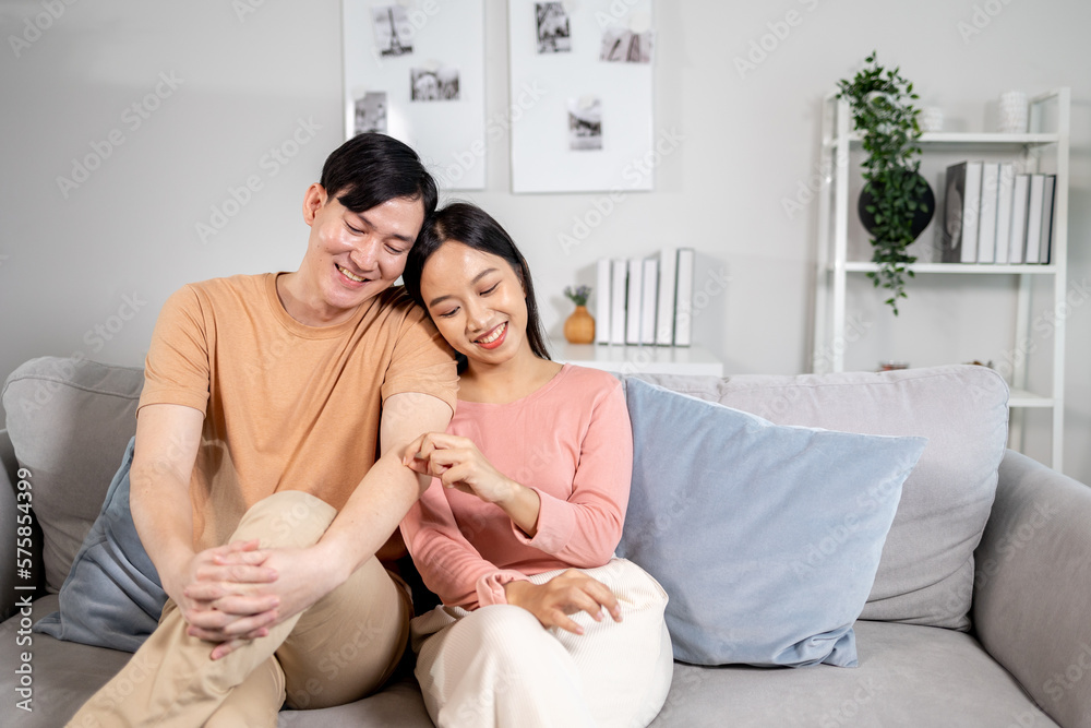 Young Asian married happy couple smiling and sitting on couch in living room at home. Boyfriend and girlfriend embracing and relaxing Young Asian married happy couple smiling and sitting on couch in living room at home. Boyfriend and girlfriend embracing and relaxing