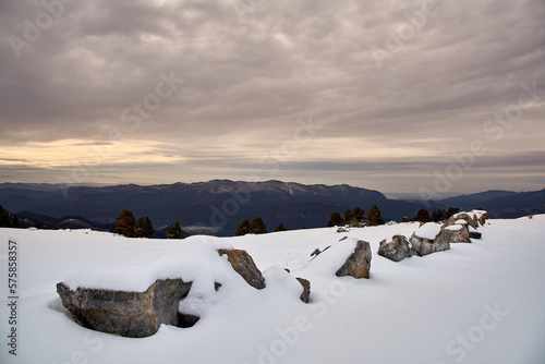 Fototapeta Naklejka Na Ścianę i Meble -  Stones surrounded by snow in vertical formation with the blurred background of mountains with a sky