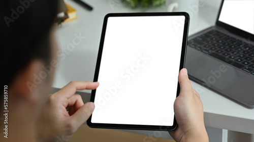 View over shoulder of man hands holding digital tablet and pointing with finger. Blank screen for webpage or advertise text