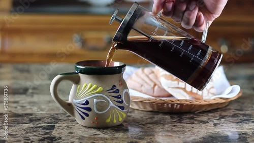 man pouring coffee from french press to traditional mexican cup in front of bread. breakfast