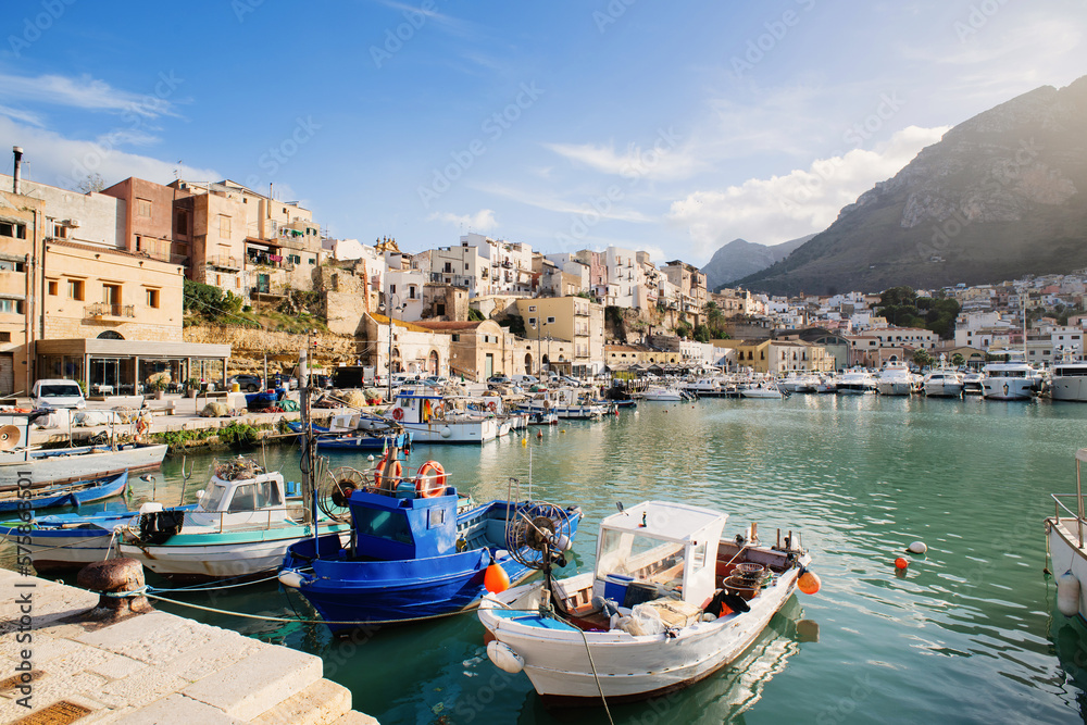 View of Castellammare del Golfo town, Sicily island, Italy. Beautiful mediterranean port with fishing boats over old town background. Popular travel destination in Europe