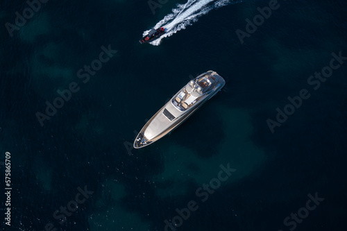Large open yacht anchored in the blue sea top view. Silver modern boat on blue transparent water aerial view. Boat fast moving next to yacht top view. © Berg