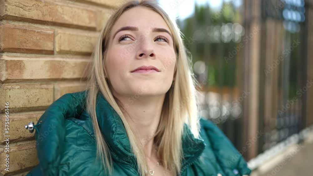 Young blonde woman standing with serious expression leaning on the wall at street Young blonde woman standing with serious expression leaning on the wall at street