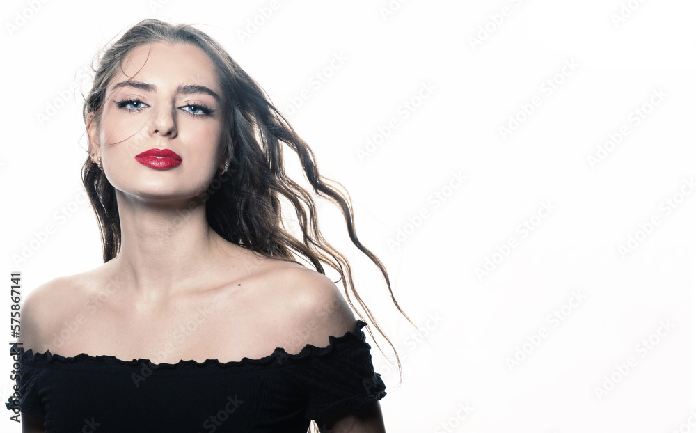 Sensual studio portrait of beautiful brunette woman with long wavy flying hair. Model with red lipstick wearing black blouse and looking at camera. White studio background. Toned image with blue color