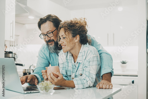 Love modern couple man and woman using together a laptop in the kitchen at home. Online computer leisure activity people. Happy family people enjoy time and surfing the web on computer. Real life