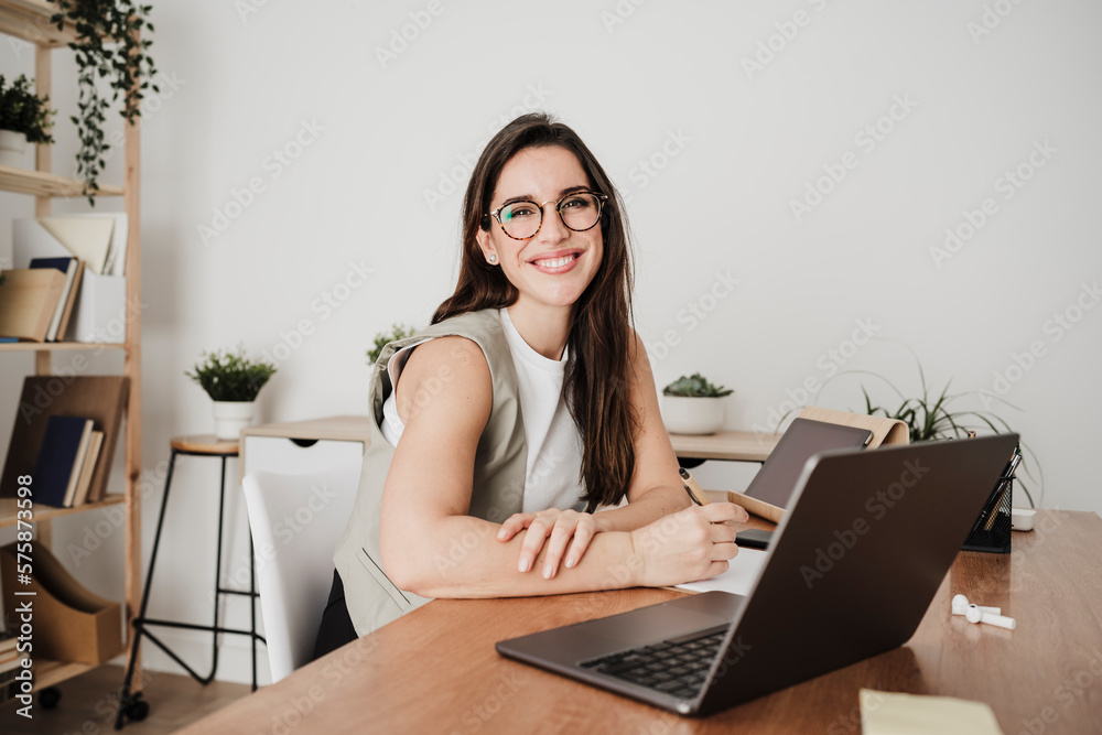 Happy businesswoman sitting in front of laptop at office desk Happy businesswoman sitting in front of laptop at office desk