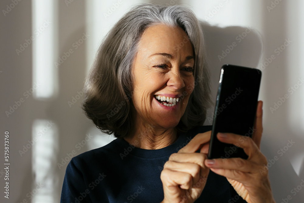 Smiling mature woman using smart phone in front of wall Smiling mature woman using smart phone in front of wall