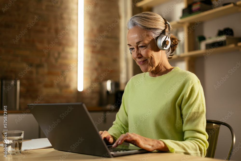 Smiling freelancer wearing wireless headphones using laptop at desk