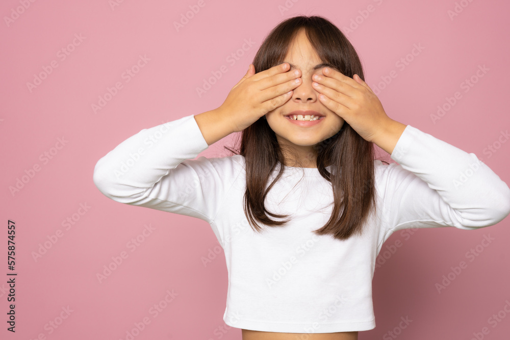 shy child who is ashamed of his bad behavior without showing his tears. a little girl covering her face with her hands is afraid of a horror movie on pink background. Body language