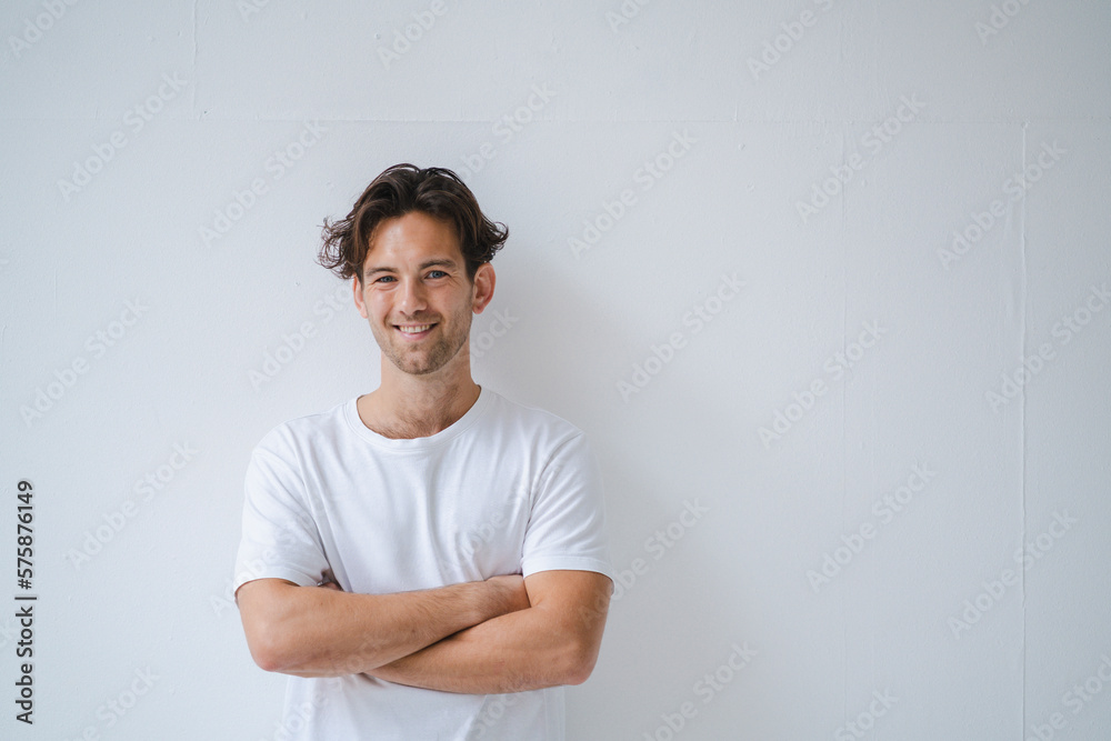 Smiling man standing with arms crossed in front of white wall Smiling man standing with arms crossed in front of white wall