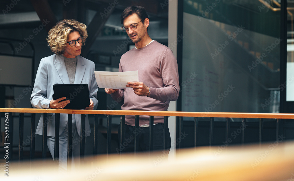 Business people reading a document together. Two professionals analyse a financial report in an office - obrazy, fototapety, plakaty 