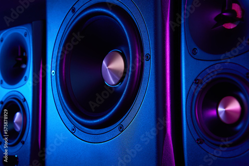 Two sound speakers and subwoofer on dark background with neon lights. Set for listening music. Audio equipment photo