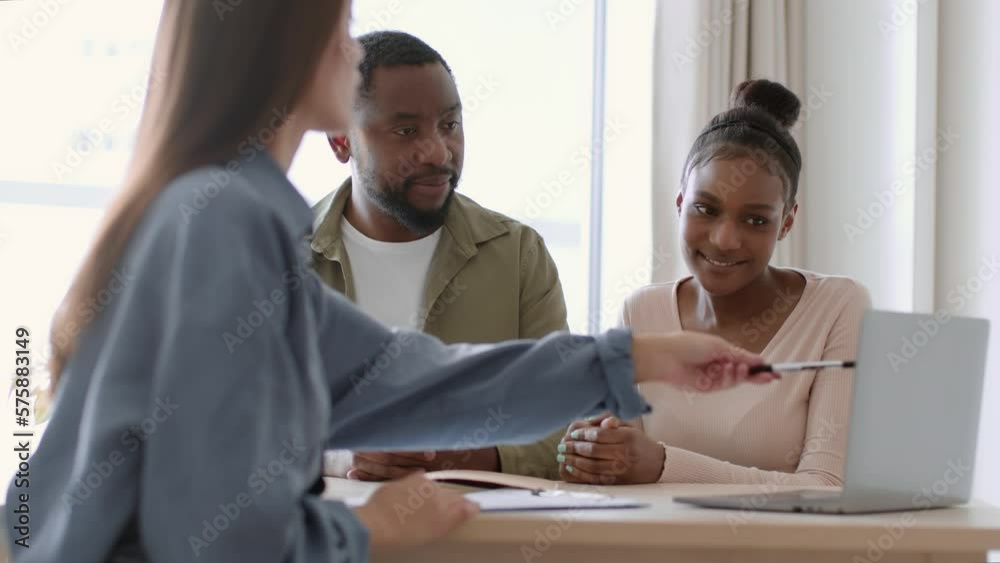 Young african american couple sitting at real estate office and discussing variants to rent on laptop, tracking shot Young african american couple sitting at real estate office and discussing variants to rent on laptop, tracking shot