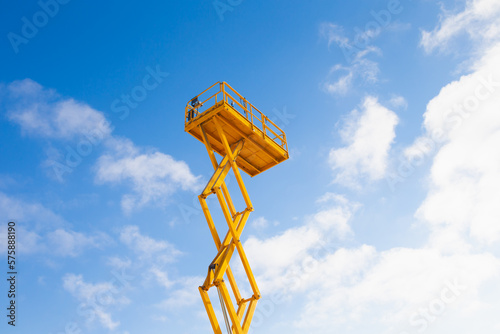 Lifted yellow scissor lift platform on blue sky background photo