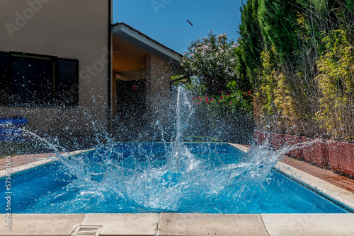 A huge splash of water is created by a cannonball dive into a swimming pool on a sunny day © Marco Taliani