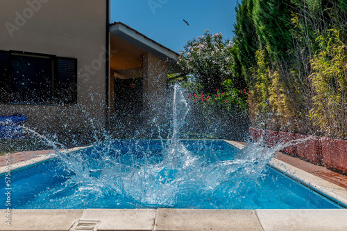 A huge splash of water is created by a cannonball dive into a swimming pool on a sunny day