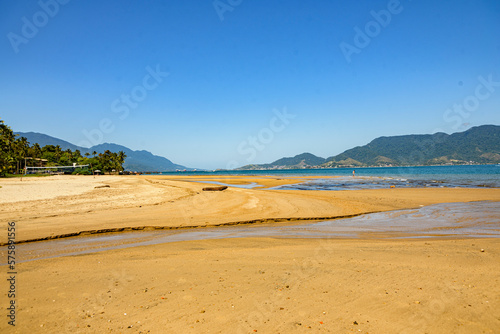 Deserted beach, large expanse of sand cut by a creek, a log on the strip of sand with textures and a mountain in the background, Ilhabela, São Paulo
