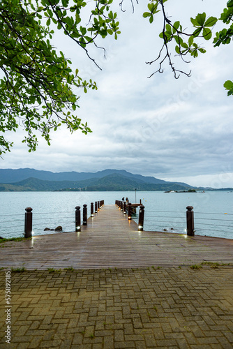 View from the pier in Praia Grande, Ilhabela, cloudy sky, trees and mountains in the background